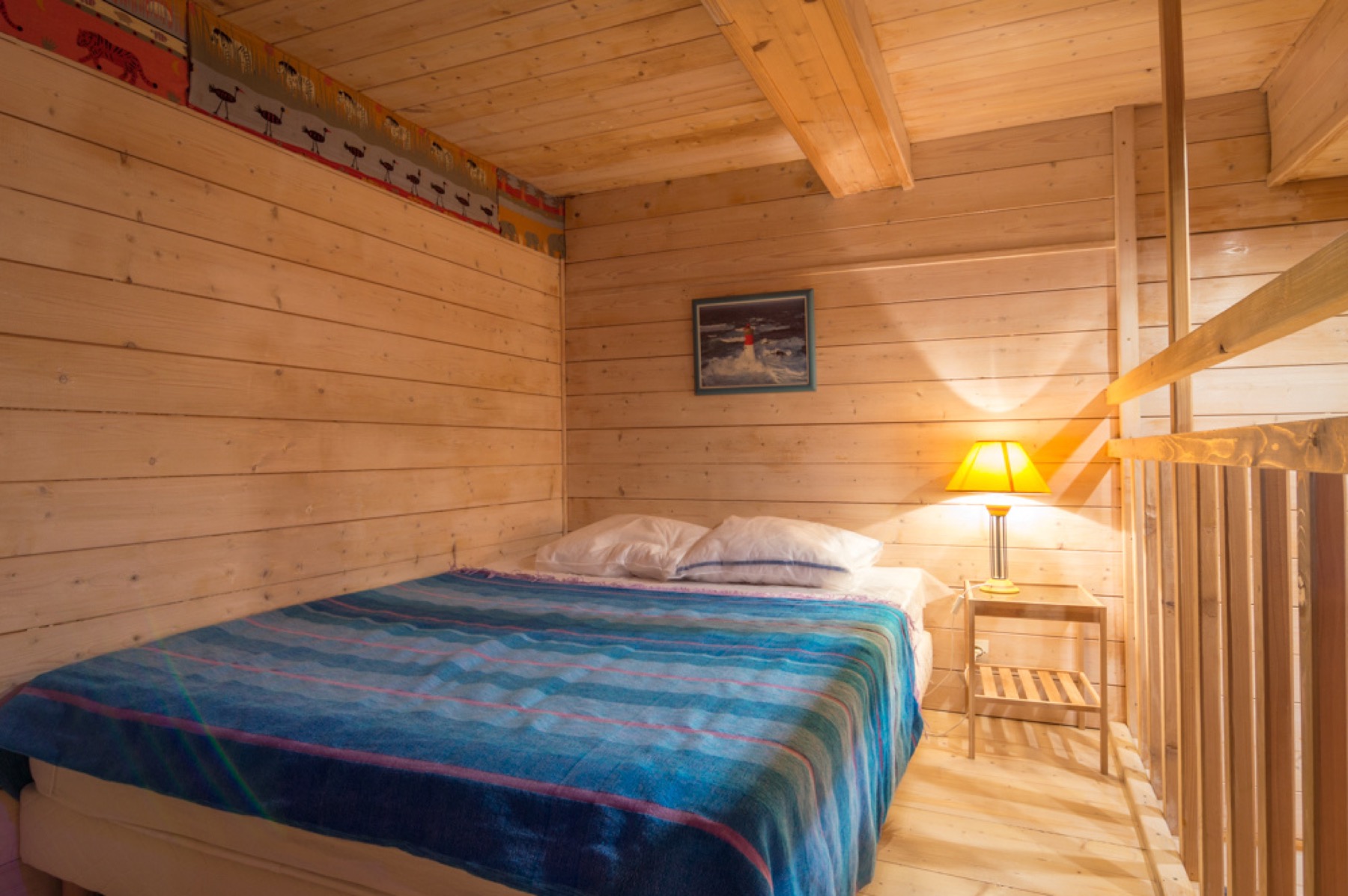 Chambre en bois avec lit double, lampe de chevet et rambarde
